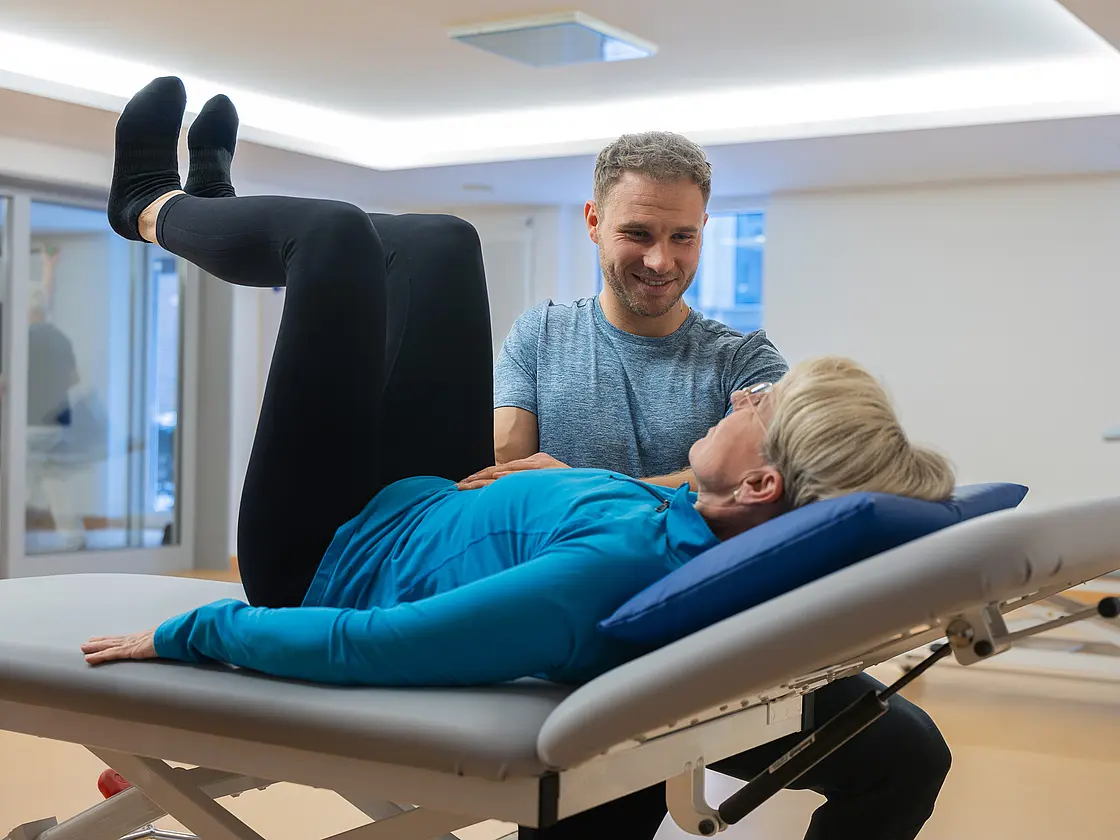 Ein Physiotherapeut unterstützt einen Patienten bei einer Übung im Therapieraum.