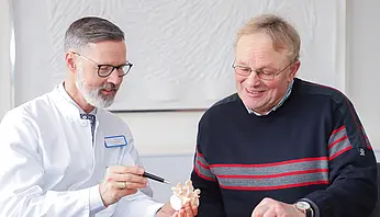 Chefarzt Dr. Christian Brinkmann erklärt einem Patienten anhand eines Wirbelsäulenmodells einen medizinischen Befund.