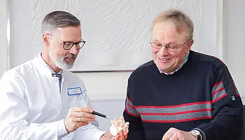 Chefarzt Dr. Christian Brinkmann erklärt einem Patienten anhand eines Wirbelsäulenmodells einen medizinischen Befund.