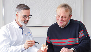 Chefarzt Dr. Christian Brinkmann erklärt einem Patienten anhand eines Wirbelsäulenmodells einen medizinischen Befund.