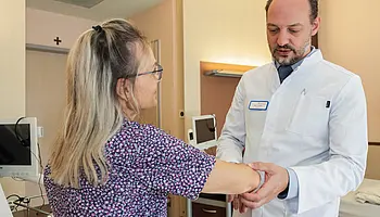 PD Dr. med. Peter Korsten hält den Unterarm einer Patientin und führt eine medizinische Untersuchung durch.