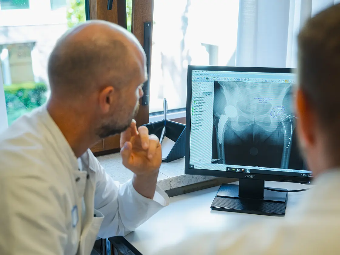 Zwei Ärzte sitzen an einem Schreibtisch und betrachten medizinische Informationen auf einem Computerbildschirm.