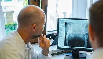 Ärzte betrachten gemeinsam eine Röntgenaufnahme eines Hüftgelenks auf einem Monitor.