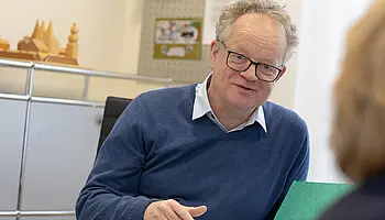 Ein Chefarzt der Schmerzklinik Herbert Thier sitzt an einem Schreibtisch und spricht mit einer Patientin, die ihm gegenübersitzt.