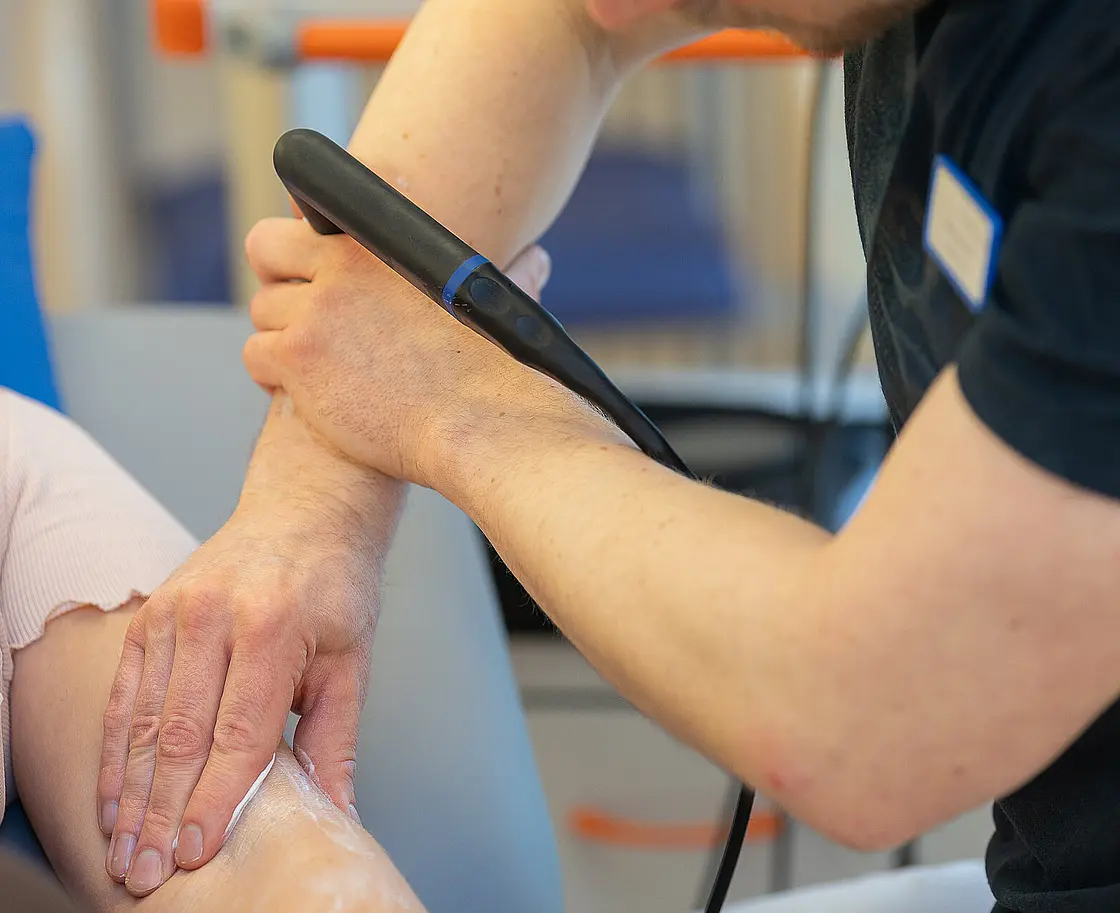 Ein Therapeut führt eine physikalische Therapie mit einem INDIBA-Gerät am Arm einer Patientin durch.