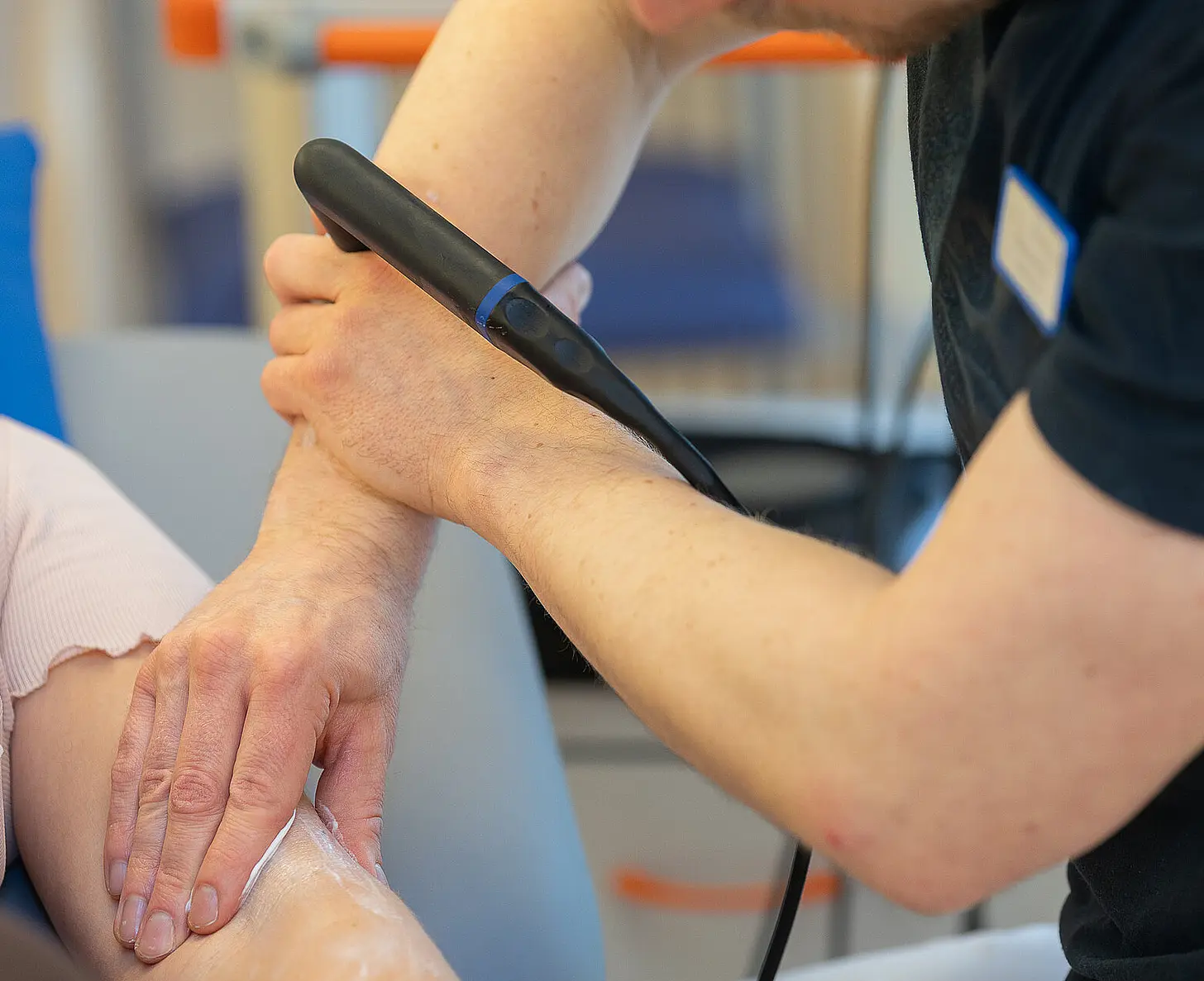 Ein Therapeut führt eine physikalische Therapie mit einem INDIBA-Gerät am Arm einer Patientin durch.