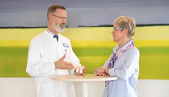 Chefarzt Dr. Brinkmann und Patientin stehen an einem Tisch und betrachten gemeinsam ein kleines Wirbelsäulenmodell.