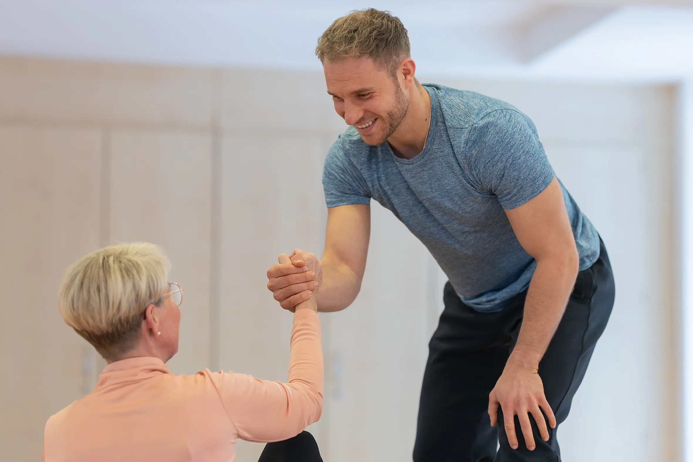 Ein Therapeut unterstützt eine Patientin beim Aufstehen und stabilisiert sie mit einem Handgriff.