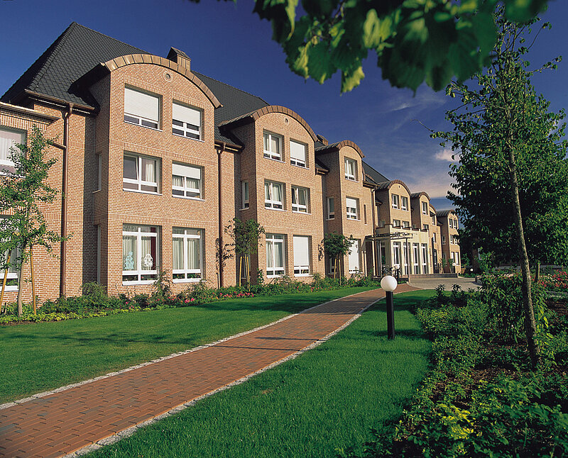 Außenansicht eines historischen Backsteingebäudes mit Gartenanlage und Gehweg.