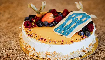 Runder Kuchen mit heller Glasur, frischen Beeren und dekorativem Element auf einer Tortenplatte.