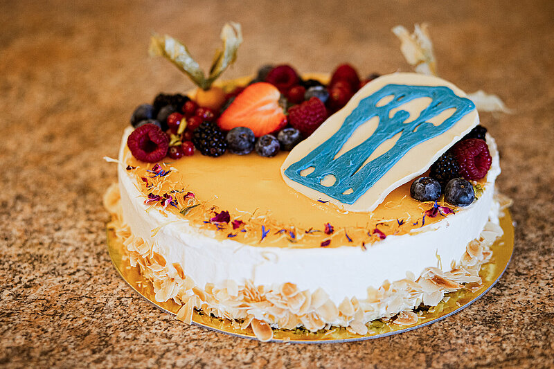 Runder Kuchen mit heller Glasur, frischen Beeren und dekorativem Element auf einer Tortenplatte.