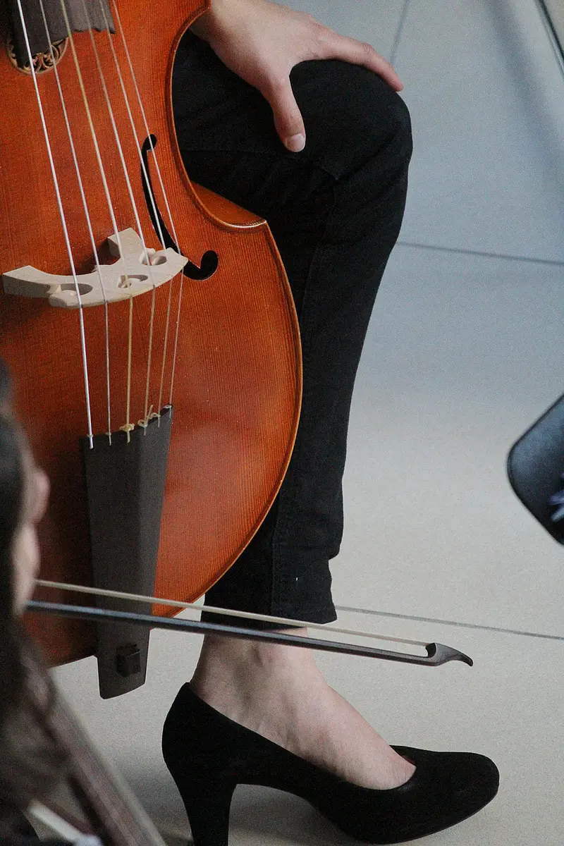 Person sitzt auf einem Stuhl und spielt ein Streichinstrument; ein Notenständer steht davor, weitere Stühle sind im Hintergrund erkennbar