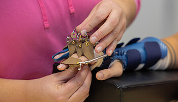 Nahaufnahme von Händen, die eine Handorthese mit Riemen und kleinen Verschlüssen an einer Hand einstellen.