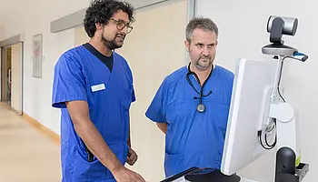 Ein Arzt und ein Intensivpfleger nutzen einen telemedizinischen Monitor zur gemeinsamen intensivmedizinischen Fallbesprechung.