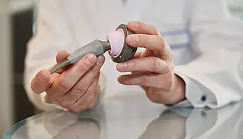 Hände in weißem Arztkittel halten eine Hüft-Implantatkomponente und zeigen deren Form und Aufbau im Detail.