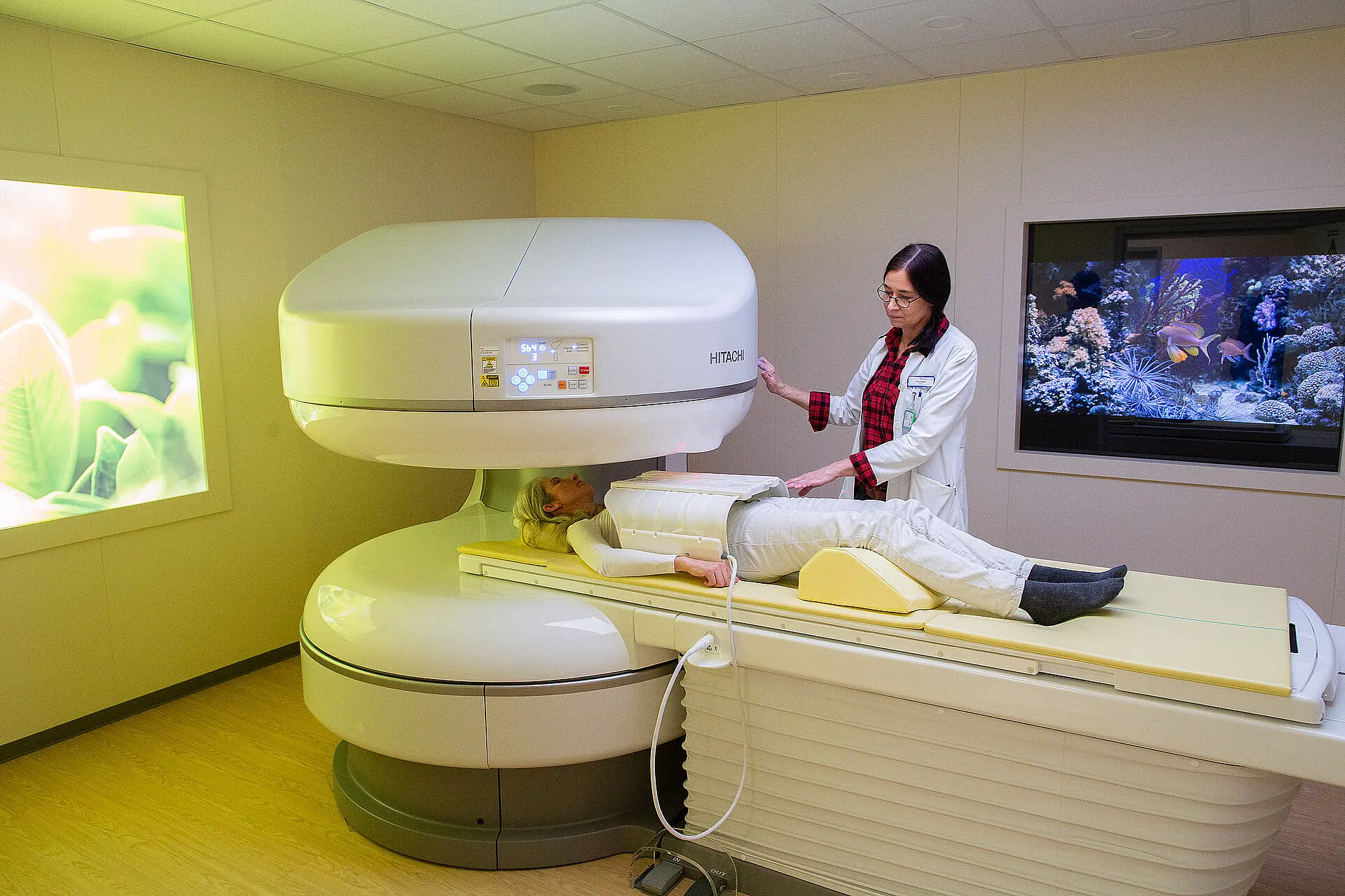 Patientin liegt auf der Untersuchungsliege eines Niedrigfeld-MRT, während eine Mitarbeiterin das Gerät seitlich bedient.