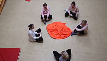 Mehrere Jugendliche sitzen im Kreis auf dem Boden um ein Tuch in der Mitte.