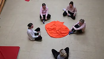 Mehrere Jugendliche sitzen im Kreis auf dem Boden um ein Tuch in der Mitte.
