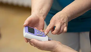 Eine Pflegefachperson hält ein medizinisches TENS Gerät in der Hand und erklärt einer Patientin dessen Bedienung.