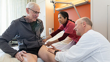 Interdisziplinäre Zusammenarbeit: Pflege und ärztlicher Dienst im gemeinsamen Austausch mit dem Patienten.