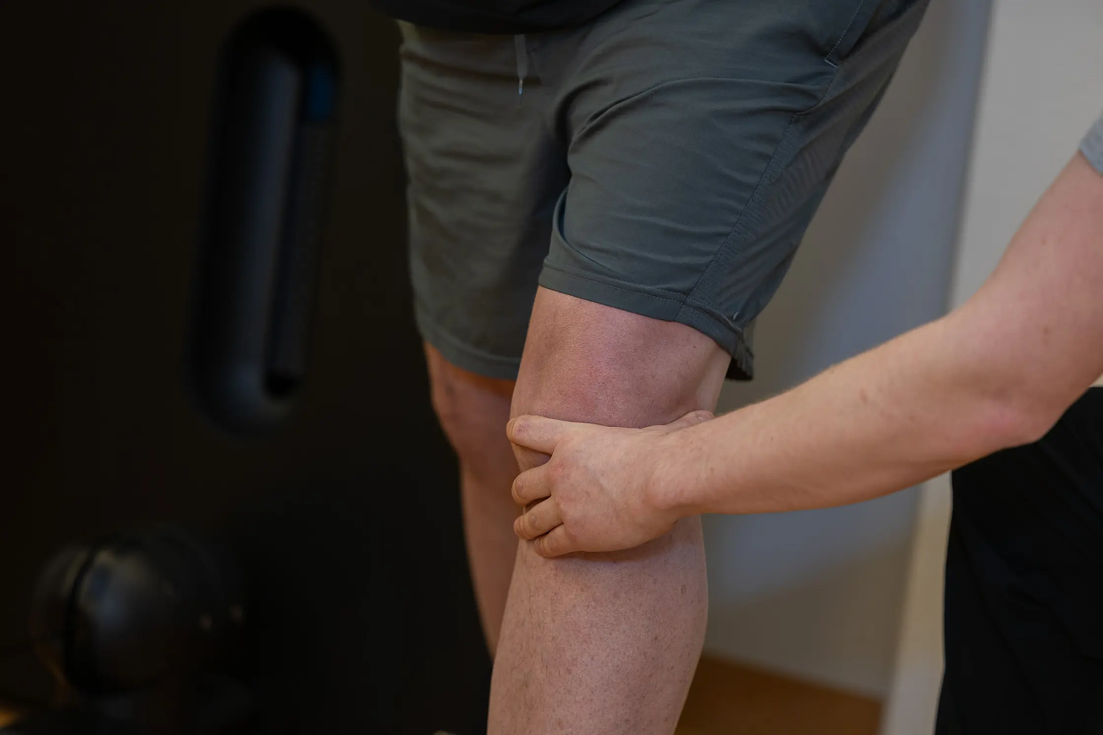 Detailaufnahme eines Therapeuten, der das Knie eines stehenden Patienten unterstützend umfasst.