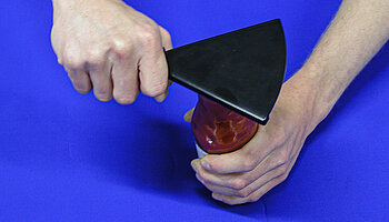 Eine Person öffnet ein Glas mithilfe eines ergonomischen Öffnungshilfsmittels mit verlängertem Hebel; durch die größere Hebelwirkung wird der Kraftaufwand in Hand- und Fingergelenken reduziert.