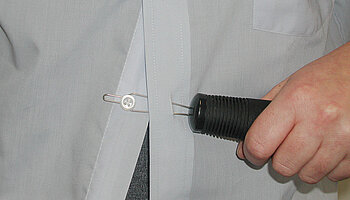Nahaufnahme einer Hand, die mithilfe einer Knöpfhilfe einen Hemdknopf durch das Knopfloch zieht; das Hilfsmittel unterstützt Menschen mit eingeschränkter Handfunktion beim selbstständigen An- und Auskleiden und schont die Gelenke.