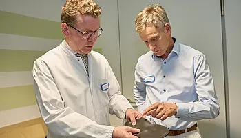 Dr. med. Ansgar Platte betrachtet zusammen mit einem Mitarbeiter der Orthopädischen Werkstatt eine orthopädische Einlage oder Schiene.