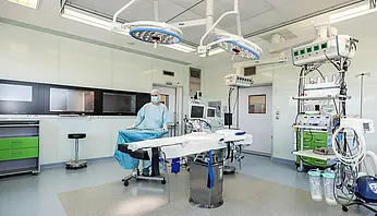 Leerer Operationssaal mit OP-Tisch, Deckenleuchten, Monitoren und medizinischen Geräten.