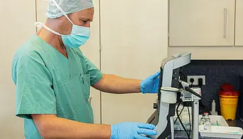 Mitarbeiter in OP-Kleidung stellt Einstellungen an einem medizinischen Überwachungsgerät ein.