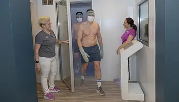 Zwei leicht bekleidete Personen verlassen eine Kältekammer, begleitet von zwei Mitarbeitenden im Vorraum.