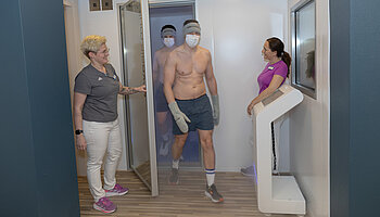 Zwei leicht bekleidete Personen verlassen eine Kältekammer, begleitet von zwei Mitarbeitenden im Vorraum.