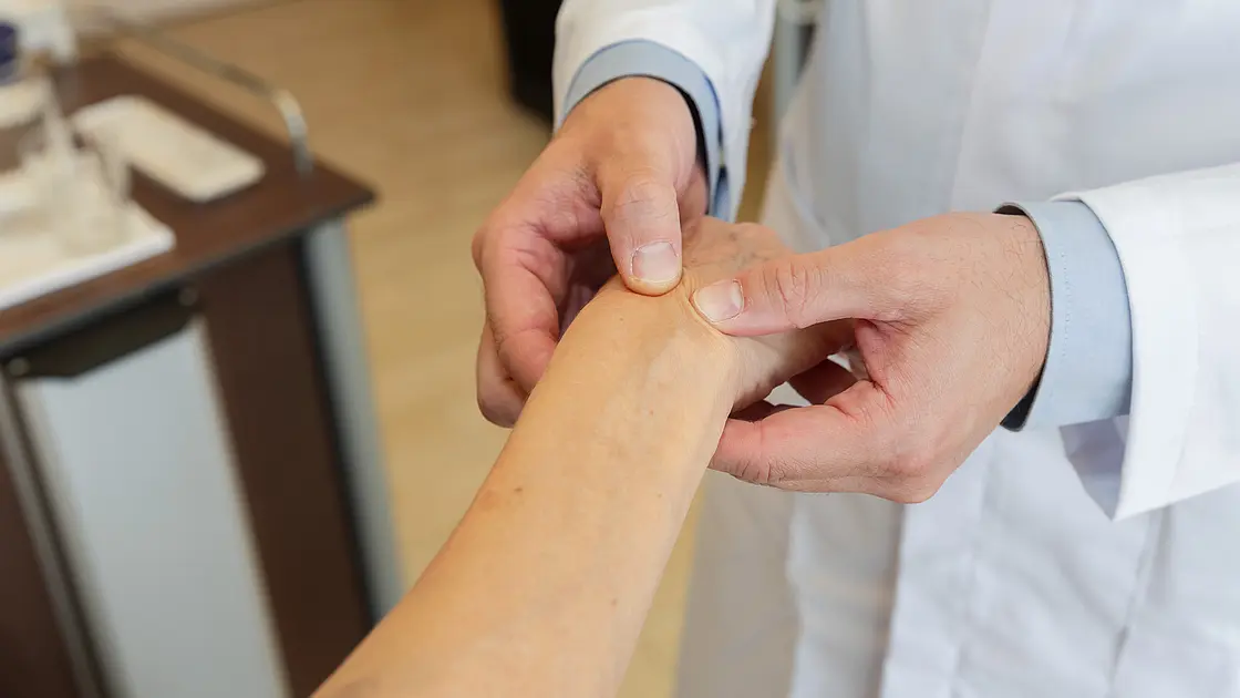 Nahaufnahme: PD Dr. med. Peter Korsten untersucht mit beiden Händen das Handgelenk einer Patientin.