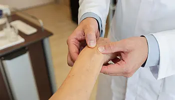 Nahaufnahme: PD Dr. med. Peter Korsten untersucht mit beiden Händen das Handgelenk einer Patientin.