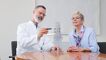 Chefarzt Dr. Brinkmann erklärt einer Patientin anhand eines transparenten Wirbelsäulenmodells den Aufbau der Wirbelsäule und das Vorgehen während der OP.