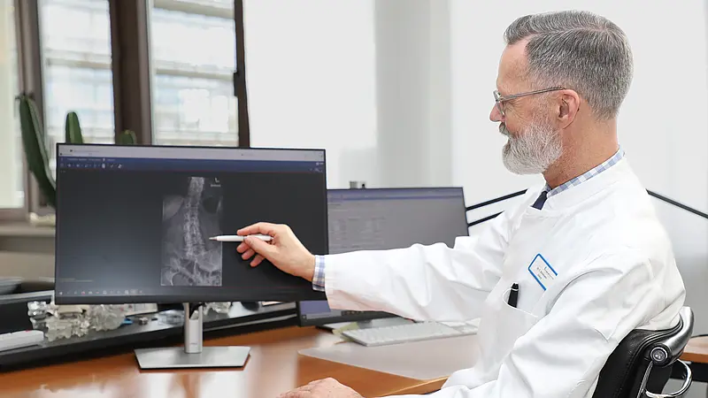 Chefarzt Dr. Christian Brinkmann zeigt auf eine Röntgenaufnahme der Wirbelsäule auf einem Computerbildschirm.