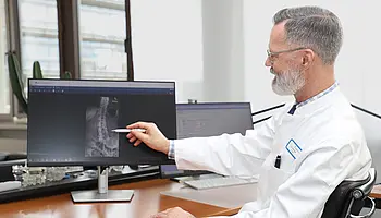 Chefarzt Dr. Christian Brinkmann zeigt auf eine Röntgenaufnahme der Wirbelsäule auf einem Computerbildschirm.