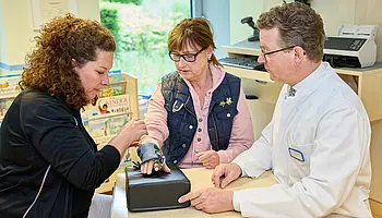 Eine Ergotherapeutin justiert eine Handorthese am Unterarm einer Patientin, während Dr. med. Ansgar Platte den Vorgang begleitet.