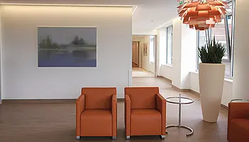 Runder Tisch mit Stühlen vor einem großformatigen Wandbild in Grüntönen, Tageslicht durch Fenster.