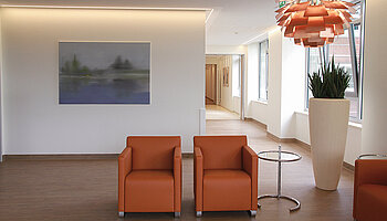 Runder Tisch mit Stühlen vor einem großformatigen Wandbild in Grüntönen, Tageslicht durch Fenster.