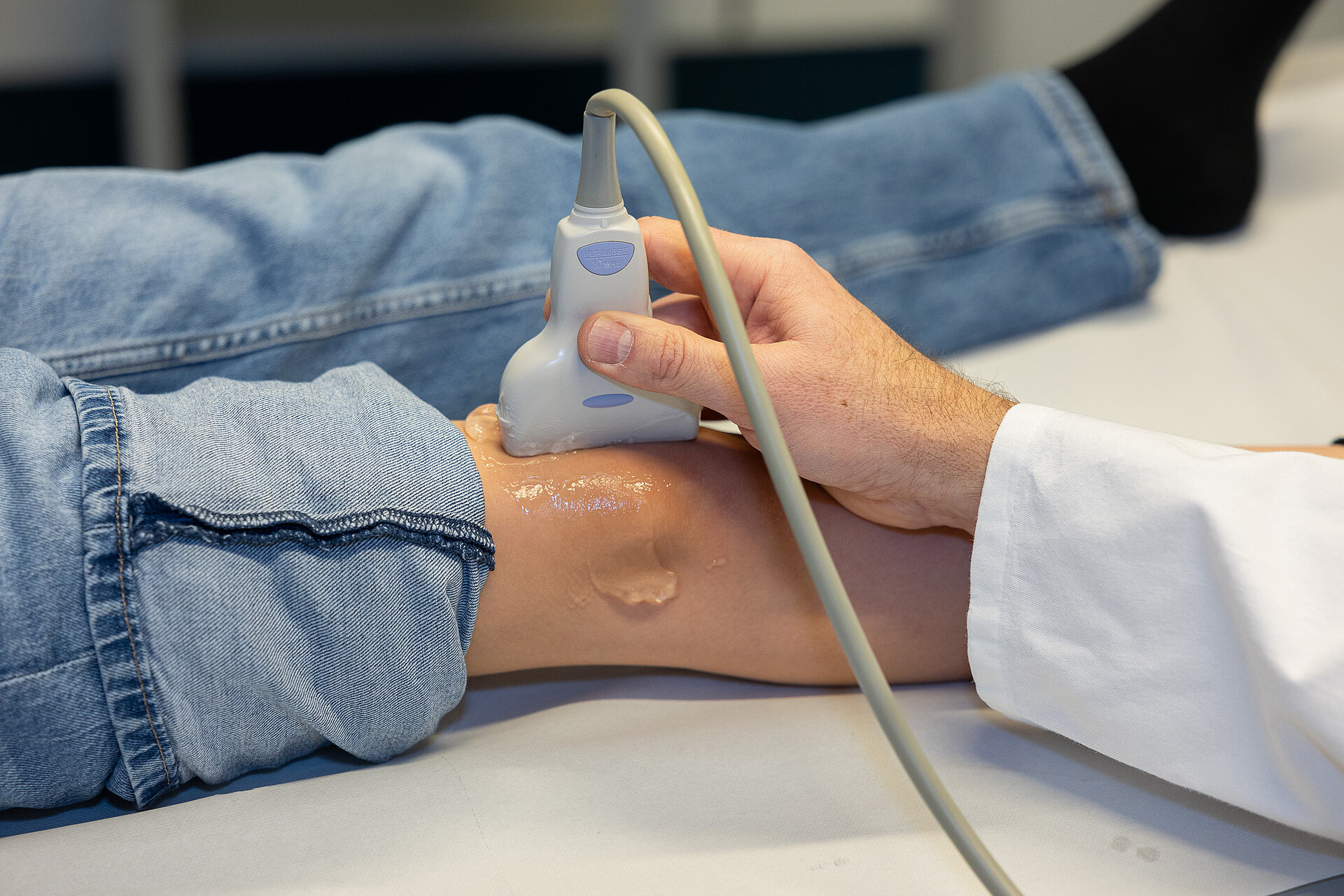 Dr. PD Daniel Windschall führt eine Ultraschalluntersuchung am Bein eines Kindes durch. Das Kind liegt entspannt auf einer Untersuchungsliege.