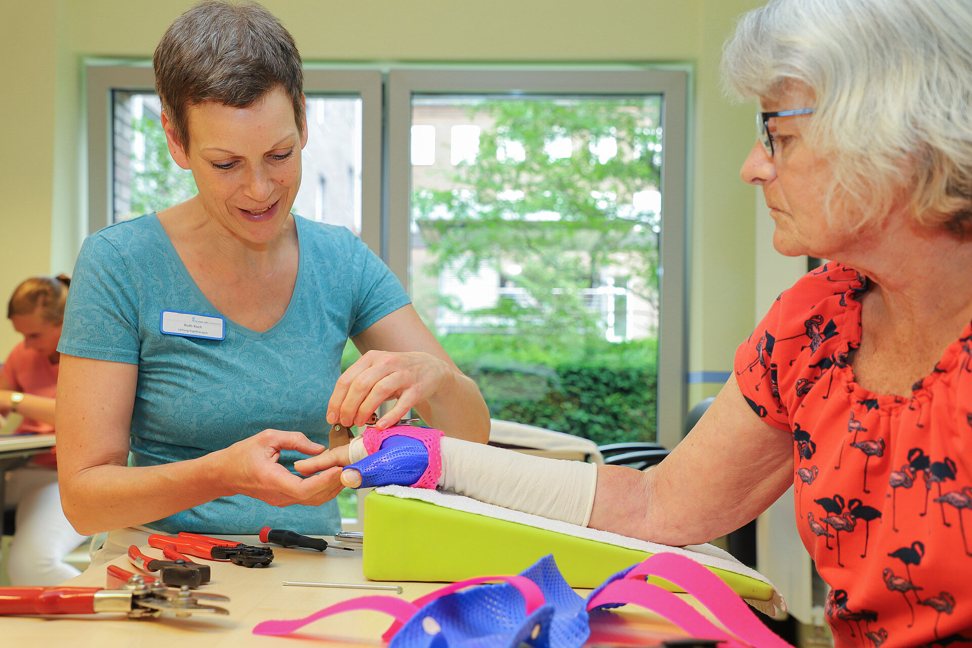 Eine Ergotherapeutin erklärt einer Patientin die Funktion einer Handschiene und prüft die Passform an der Hand.