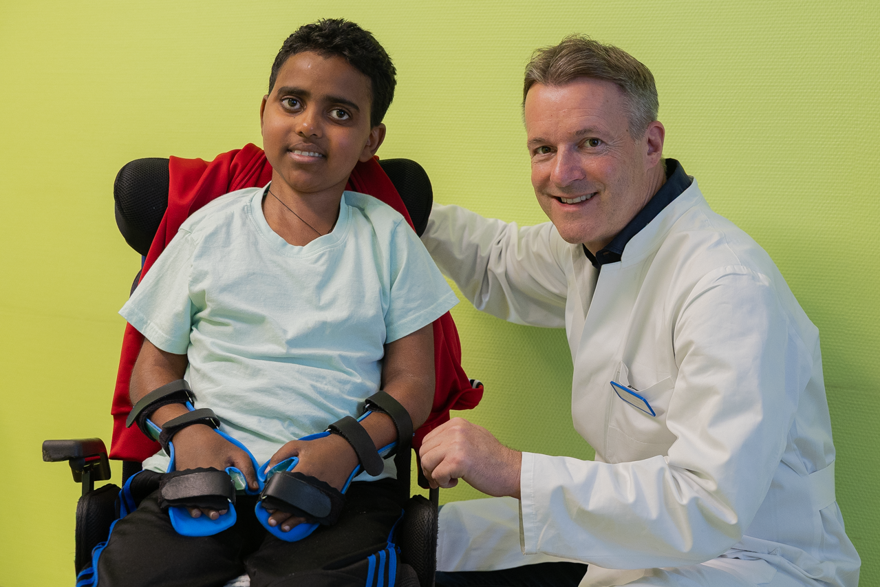 Ein eritreischer Junge in einem Rollstuhl neben seinem behandelnden Arzt.