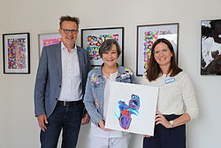 Dr. Ansgar Klemann als Vorsitzender der Geschäftsführung, verantwortliche Künstlerin Bianca Wolejszo und Alicja Skowasch, hauptamtliche Seelsorgerin (v.l.) präsentieren die Werke der Schmerzpatientin.