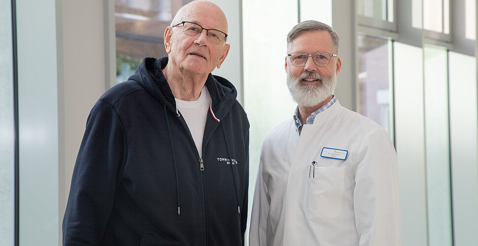 Ein Arzt und sein Patient stehen in der Magistrale und lächeln.