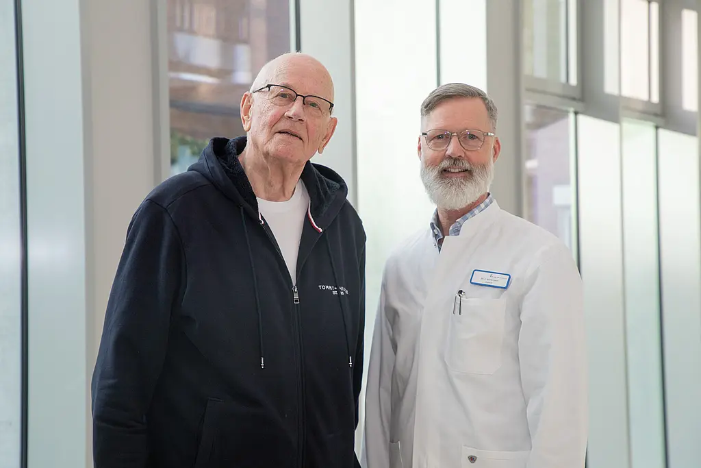 Ein Arzt und sein Patient stehen in der Magistrale und lächeln.