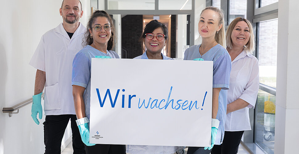 Ein Foto von hauswirtschaftliche Mitarbeiterinnen und Mitarbeitern, die ein Schild mit dem Slogan in den Händen halten.