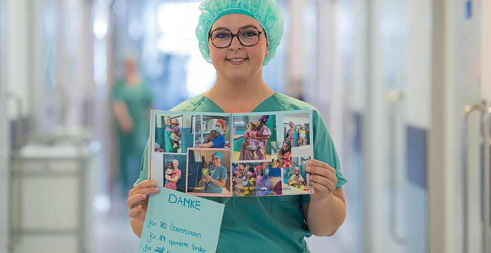 Eine Frau in OP-Kleidung steht auf einem Flur und hält ein Fotoalbum in den Händen.