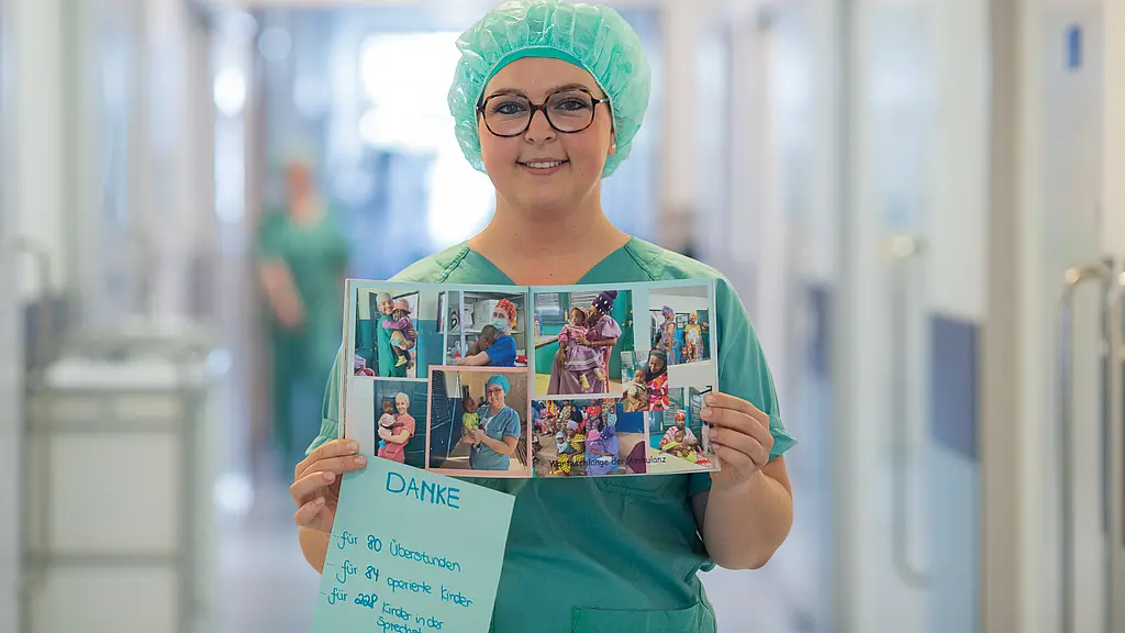 Eine Frau in OP-Kleidung steht auf einem Flur und hält ein Fotoalbum in den Händen.