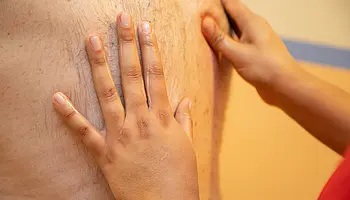 Die Hände der Masseurin beim Massieren des Rückens von einem Mann.